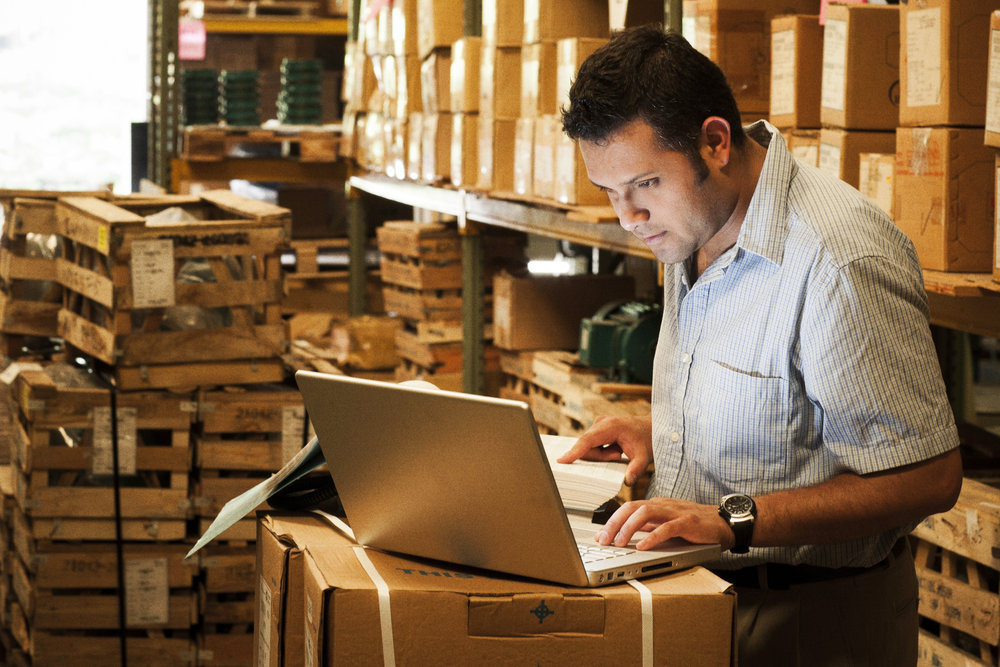 Hispanic manager working in warehouse going over inventory and shipping and receiving.