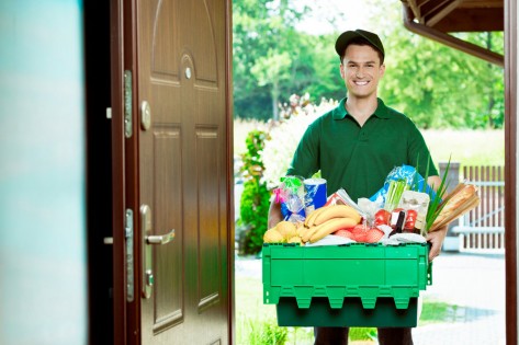 Delivery man standing at the door of the house and carrying box with groceries, smiling at camera.