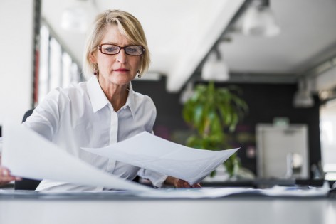 A photo of mature businesswoman examining documents at desk. Concentrated professional is analysing papers in office. Executive is in formals.