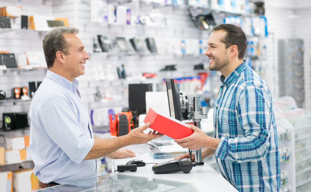 Casual man shopping at a tech store and talking to salesman over the counter