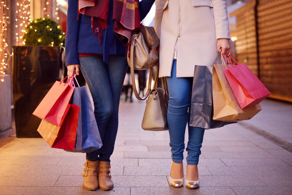 Young women shopping in the city, legs and hands close up, carrying paper bags.