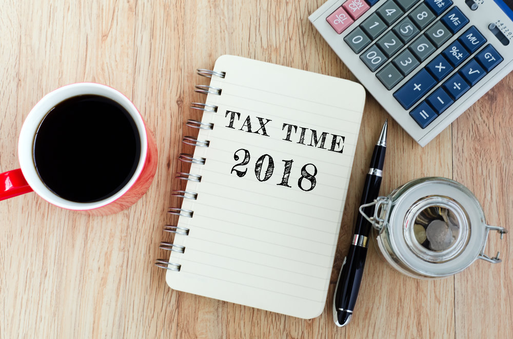 Tax Time text on notepad - coffee, jar coins, pen and calculator on top of wooden table.