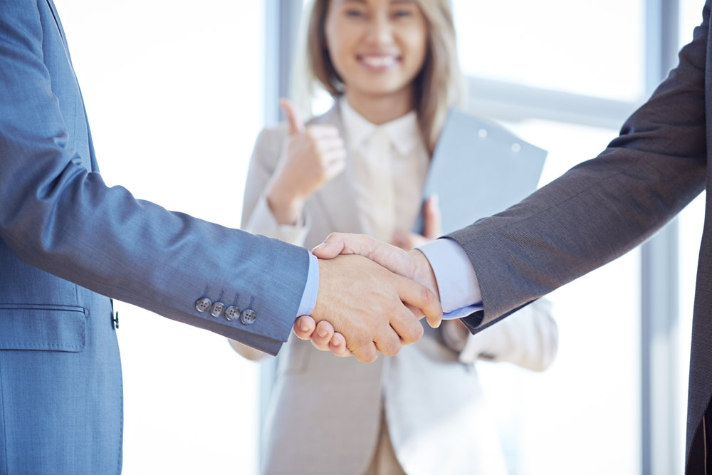 Two businessmen shaking hands, happy businesswoman giving thumbs up in the background